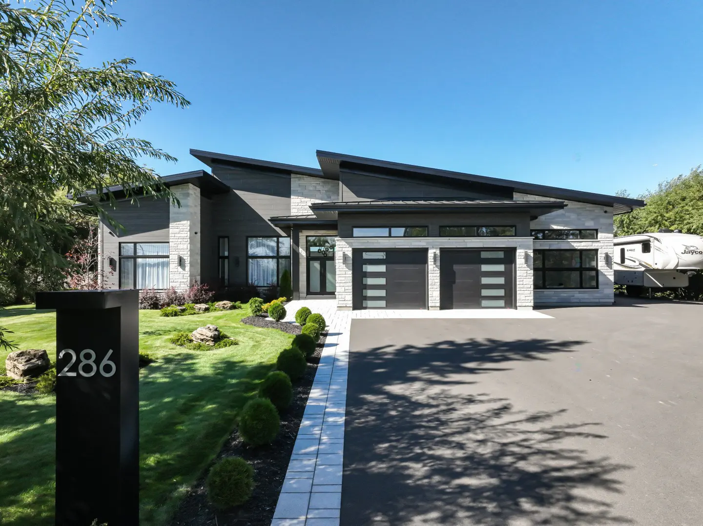 Modern house with gray siding, stone accents, and a black roof. A black mailbox with the number 286 sits on the lawn.