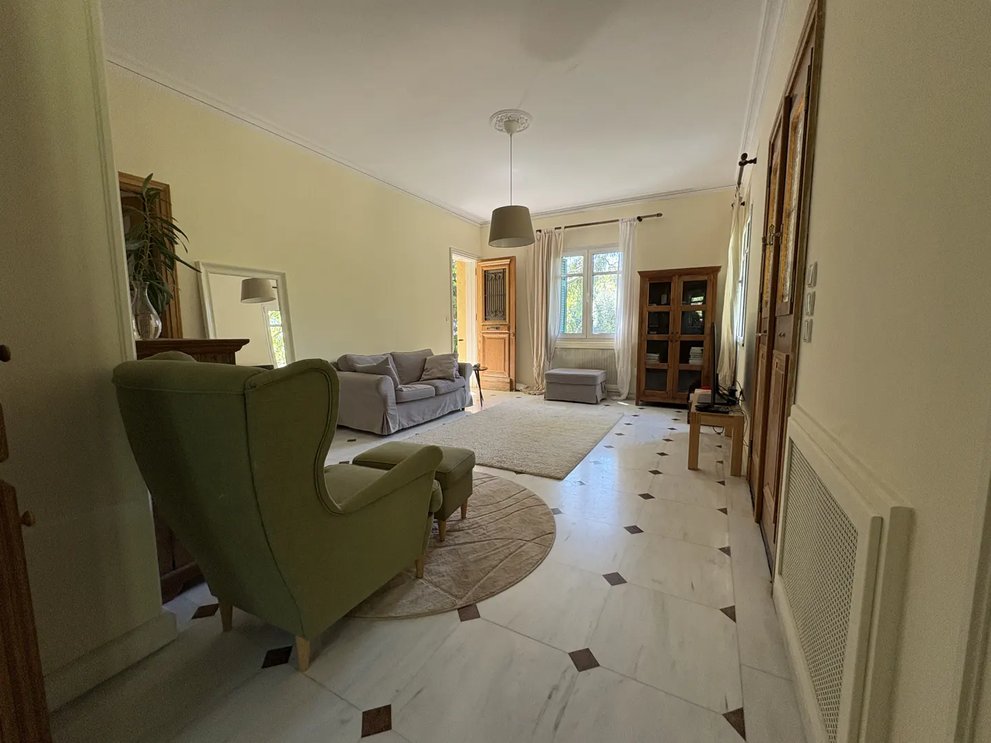Living room with marble floors, a green armchair, a gray sofa, and a wooden cabinet.