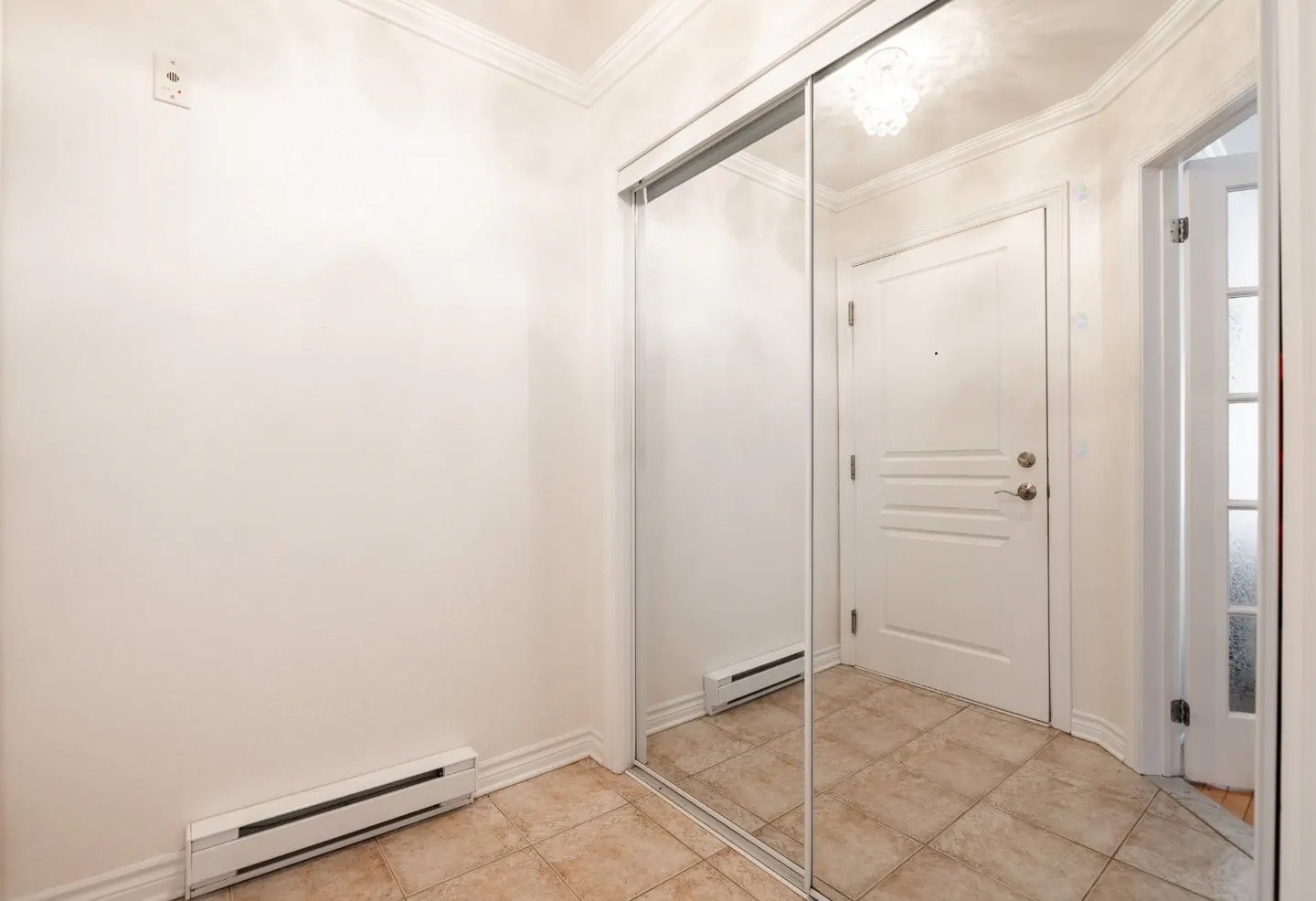 Hallway with beige tile floor, white walls, and a mirrored closet. A white door is visible in the background.