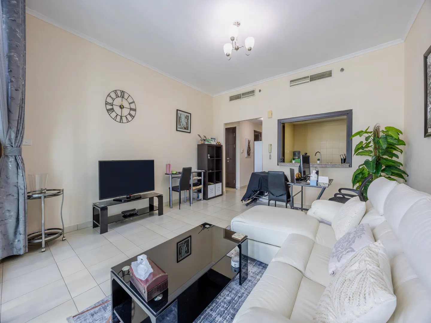 A bright living room with a white sectional sofa, black coffee table, TV, and a view into the kitchen.