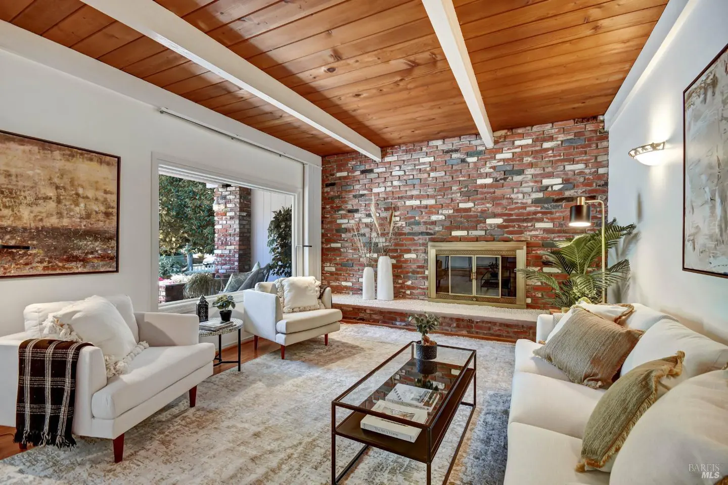 Living room with white furniture, brick fireplace, wood ceiling, and a glass coffee table on a patterned rug.