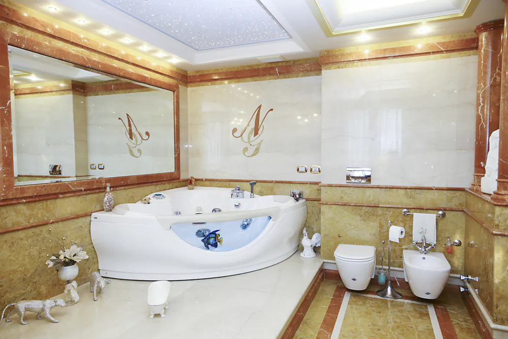 Opulent bathroom with marble walls, a large mirror, and a white jacuzzi tub with fish decorations. Toilet and bidet are visible.