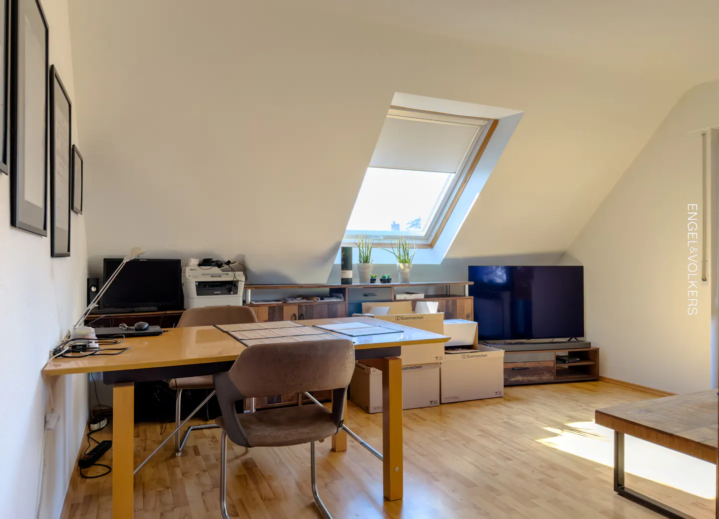 Attic room with a skylight, featuring a wooden table and chairs, a TV, and moving boxes on a light wood floor.