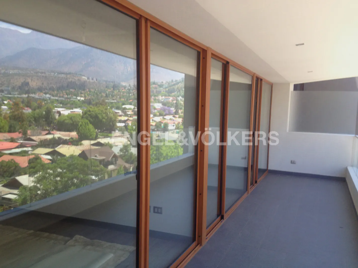 Balcony view with brown-framed sliding glass doors overlooking a town and mountains. Engel & Völkers logo visible.