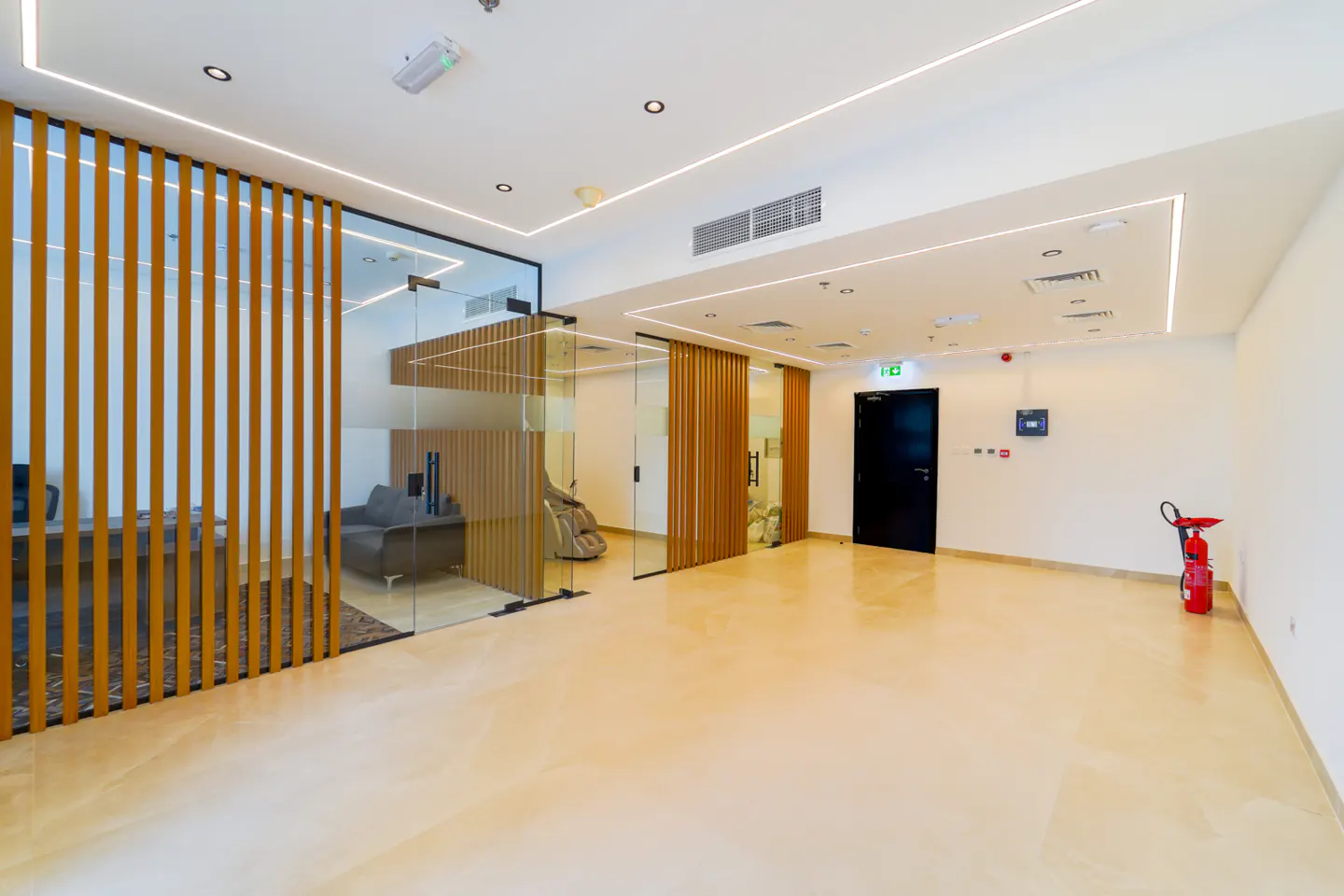 Bright office space with glass-walled rooms separated by wood slats. A black door and red fire extinguisher are visible.