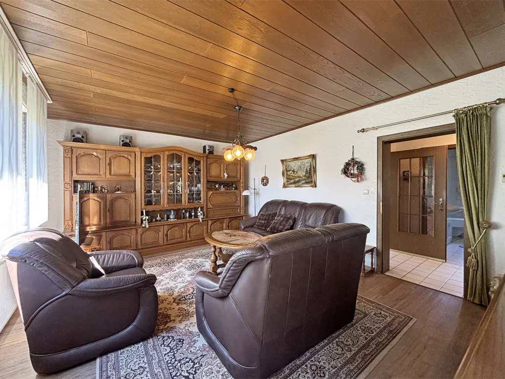 Living room with brown leather furniture, wood paneled ceiling, and a large wooden cabinet. A patterned rug covers the floor.