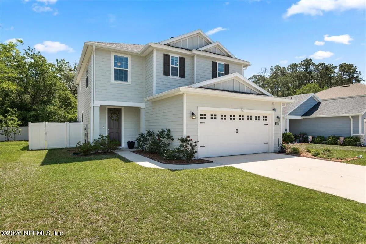 Two-story light blue house with a white garage door, dark shutters, and green lawn under a blue sky.