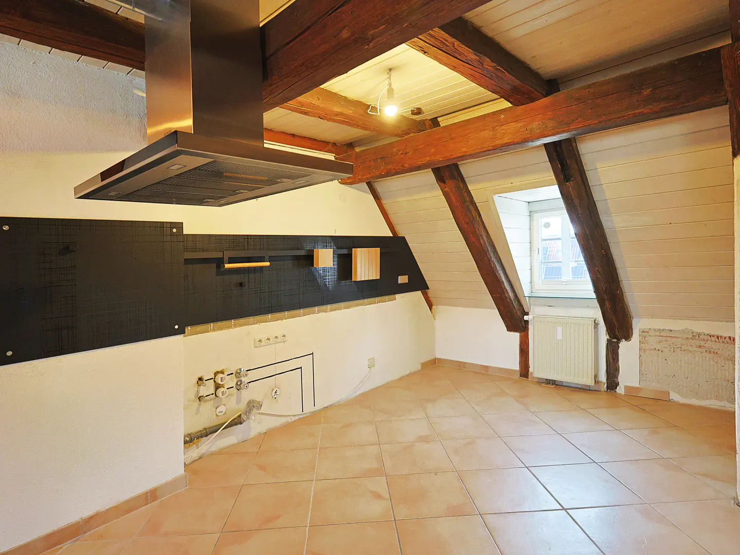 Attic room with exposed beams, a stainless steel range hood, and tan tile flooring. A window is visible in the background.