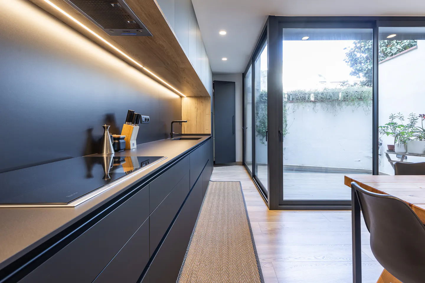 A modern kitchen with black cabinets, a wood shelf with LED lighting, and sliding glass doors to a patio.
