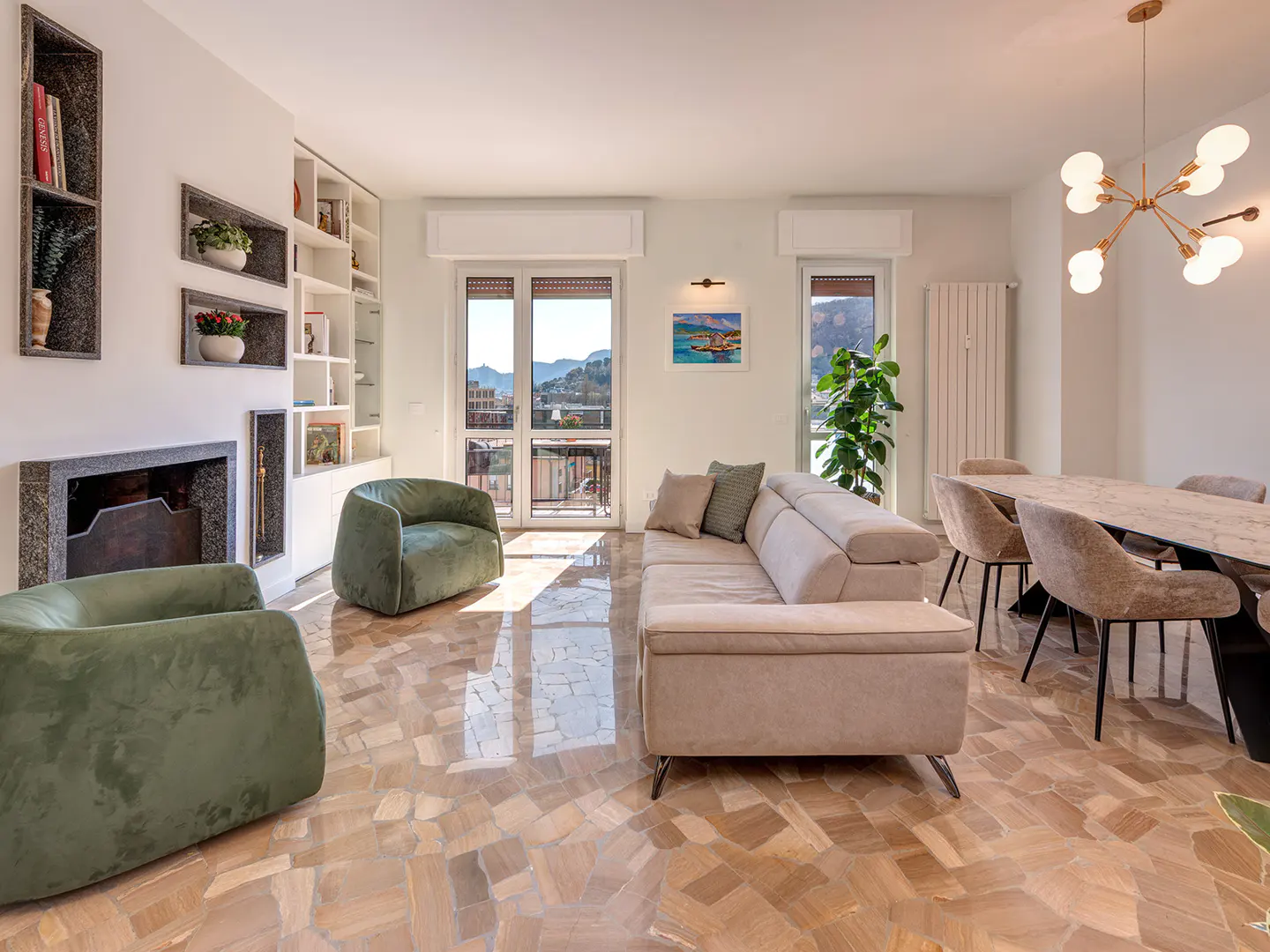Bright living room with green armchairs, beige sofa, dining table, and a view of the city from the balcony.