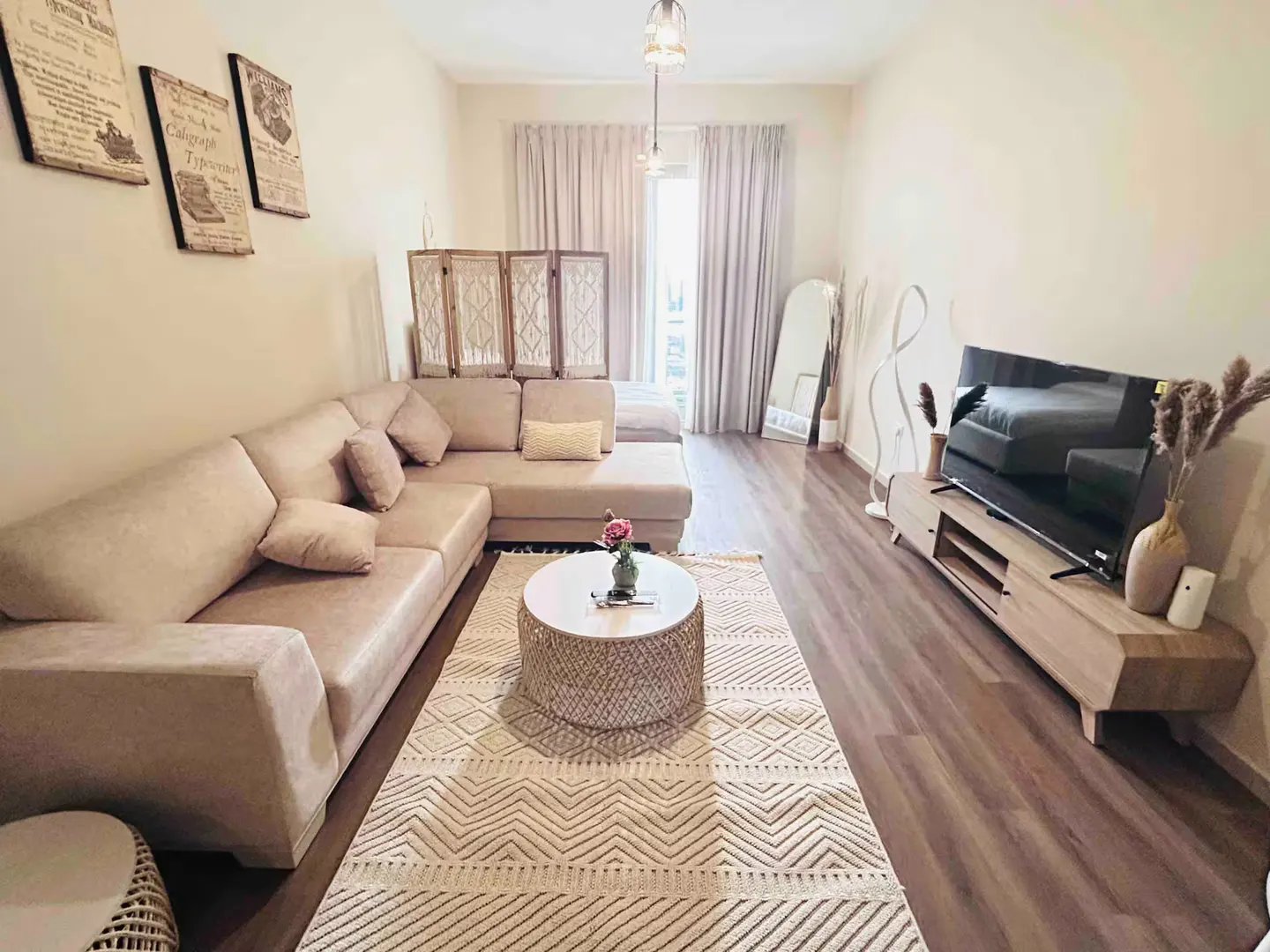Living room with beige sectional sofa, round coffee table, patterned rug, TV, and decorative items. Neutral color palette.