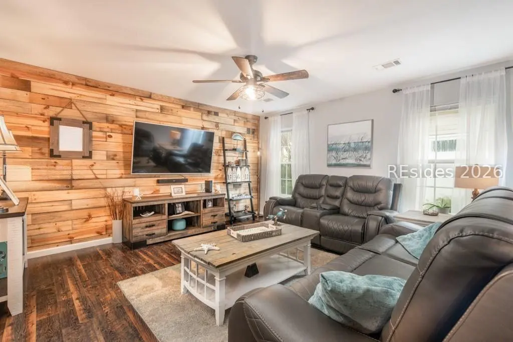 Living room with wood paneled wall, TV, leather sofas, and a white coffee table on a light rug.