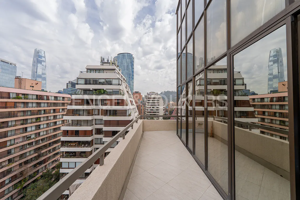 Balcony view of a city skyline with modern buildings and skyscrapers under a cloudy sky, reflected in glass windows.