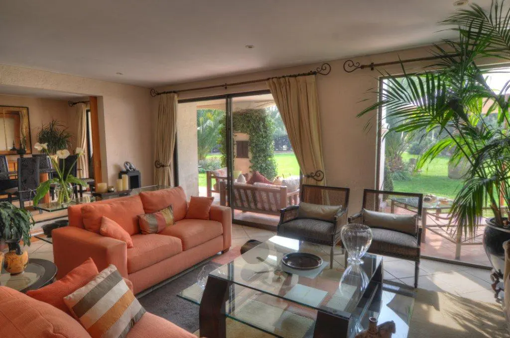 A bright living room with an orange sofa, glass table, and chairs, opening to a green lawn.
