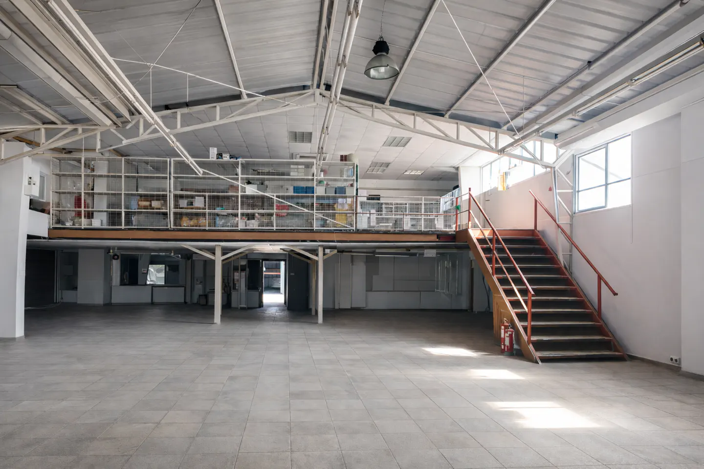 A large, empty warehouse with a mezzanine level and red stairs.