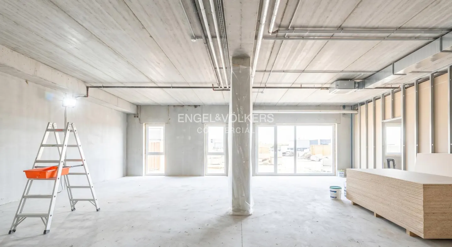 Unfinished commercial space with concrete ceiling, exposed pipes, a ladder, and a stack of plywood boards.