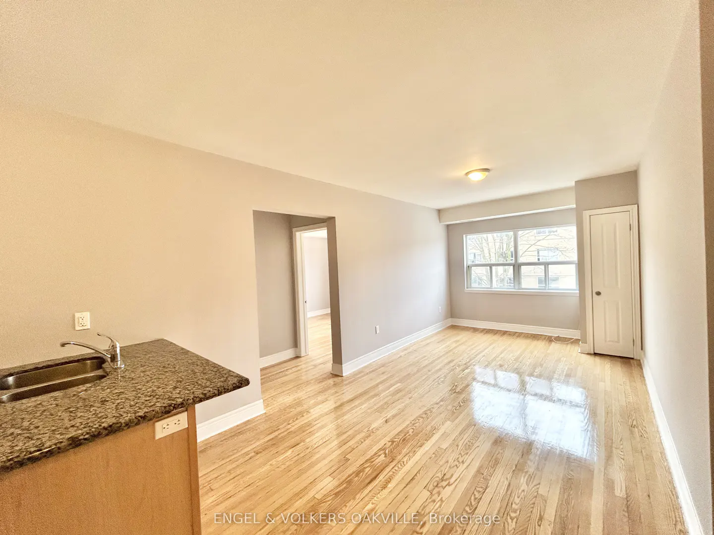 A bright, empty apartment with hardwood floors, a kitchen island, and a window.