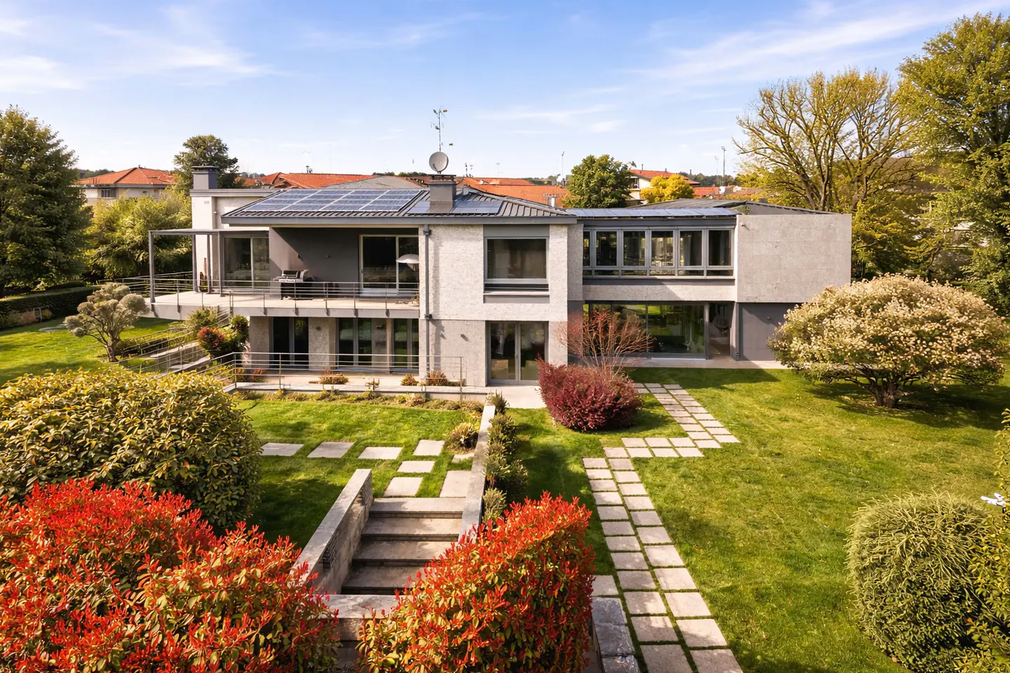 Two-story modern home with solar panels, a balcony, and a stone-paved path through a green lawn.