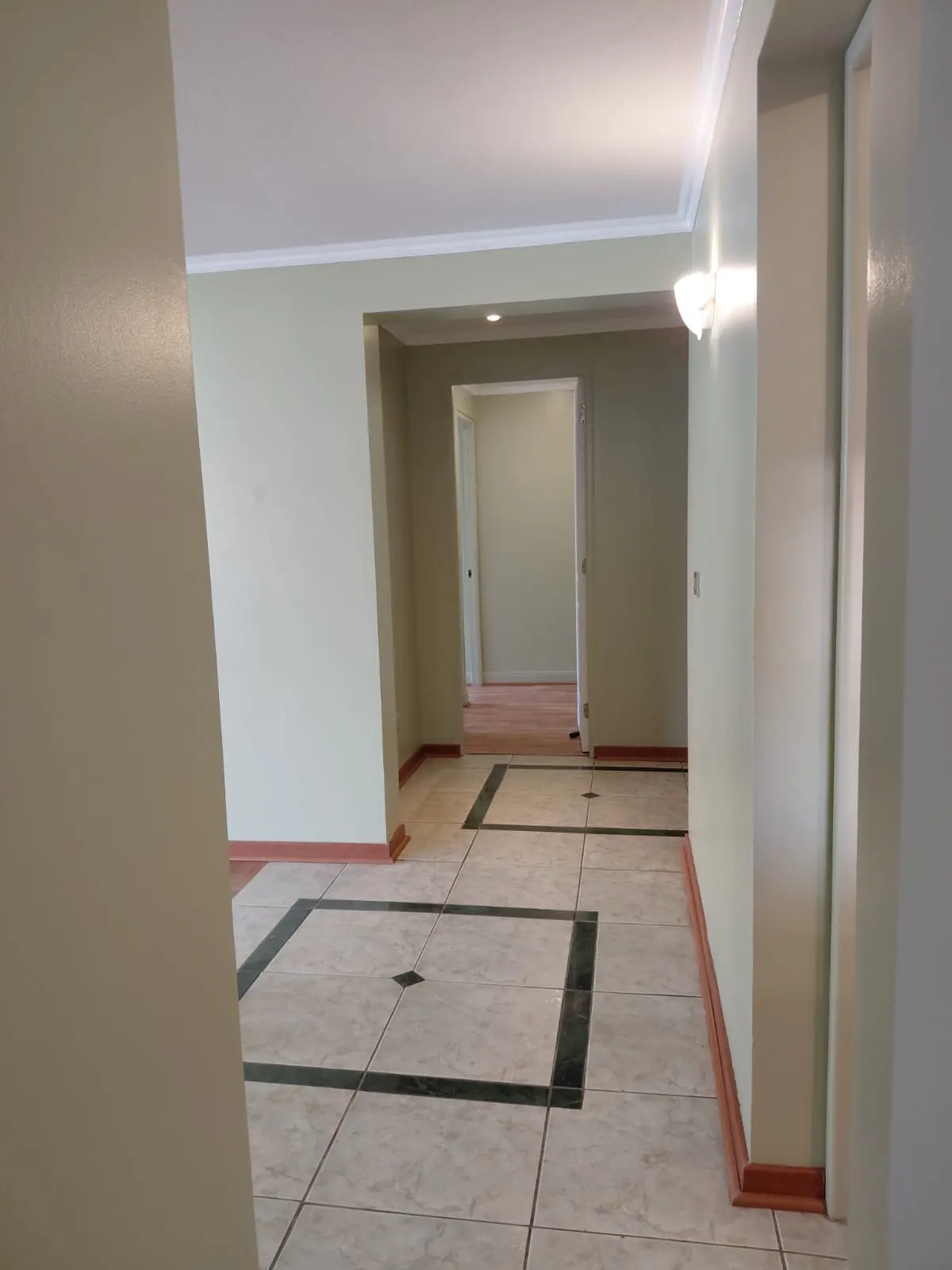 Interior view of a hallway with light green walls, white trim, and tiled floors with dark green accents. Open doorways lead to other rooms.