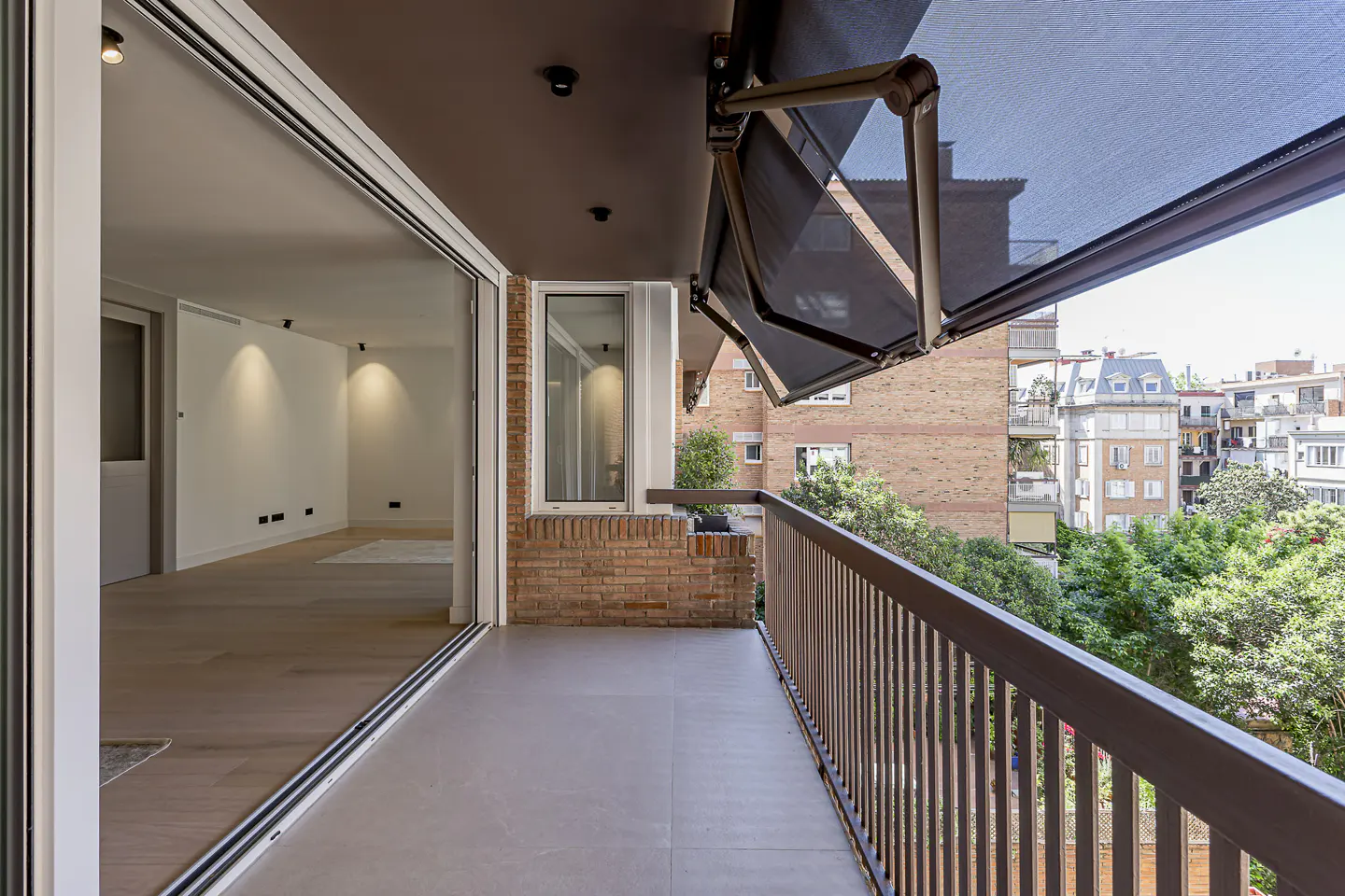 Balcony view with brown railings, a retractable awning, and a sliding glass door to a bright, modern interior. Cityscape visible.