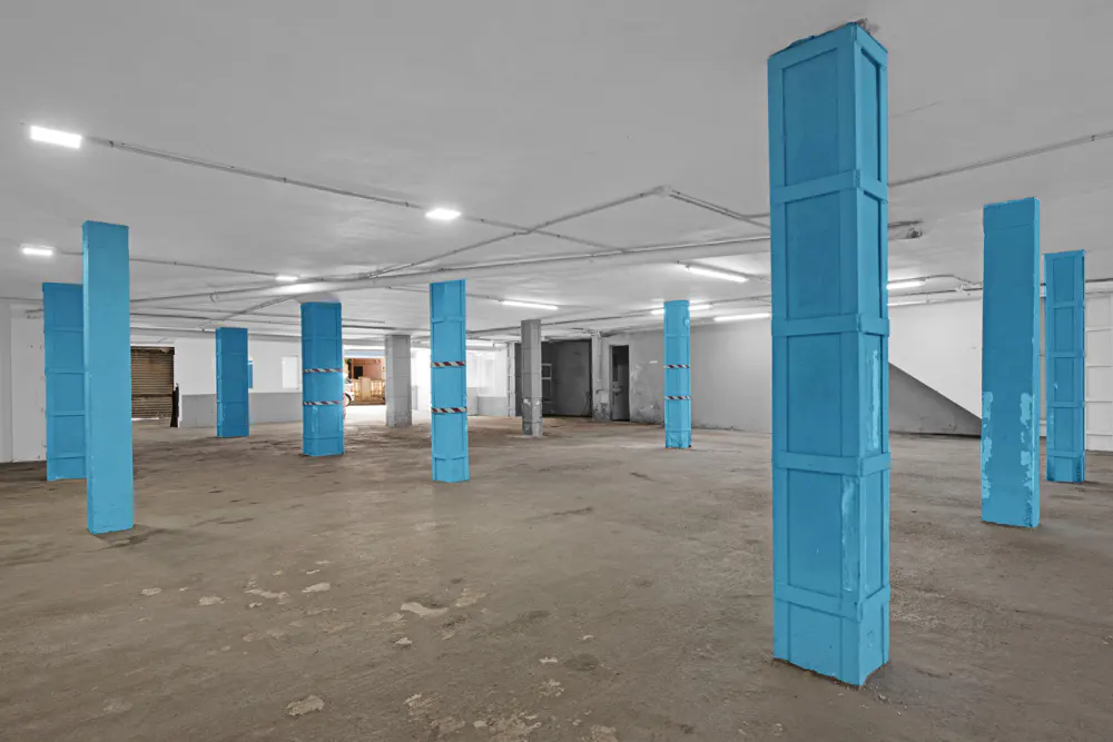 A large, empty room with blue support columns and a concrete floor.