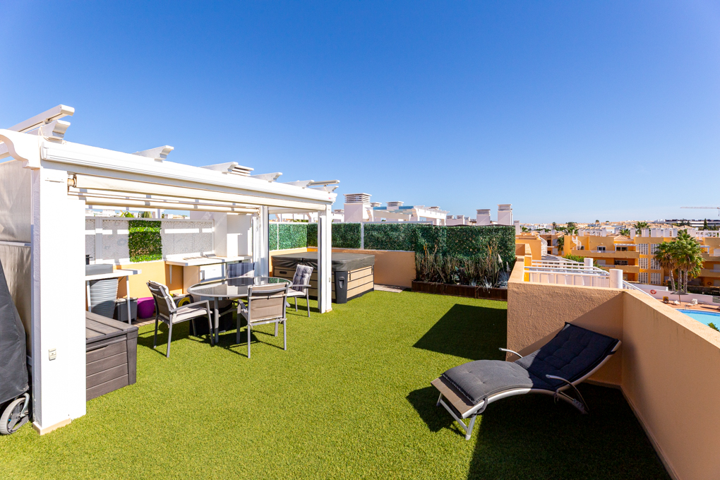 Rooftop terrace with artificial grass, dining set under a white pergola, hot tub, and a lounge chair under a clear blue sky. [AI-generated text]