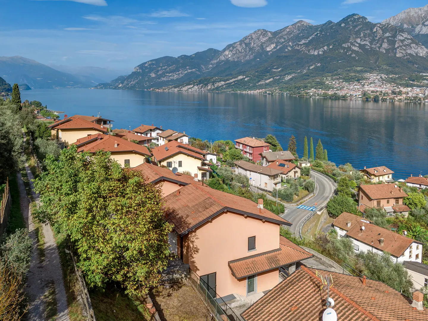 Lake Como view of hillside homes with red tile roofs, blue water, and mountains in the background.