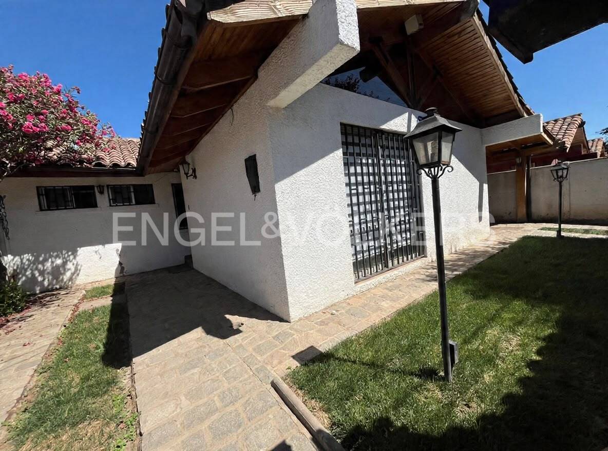 White stucco house exterior with a wooden roof, stone walkway, lawn, and a black metal lamp post under a clear blue sky.