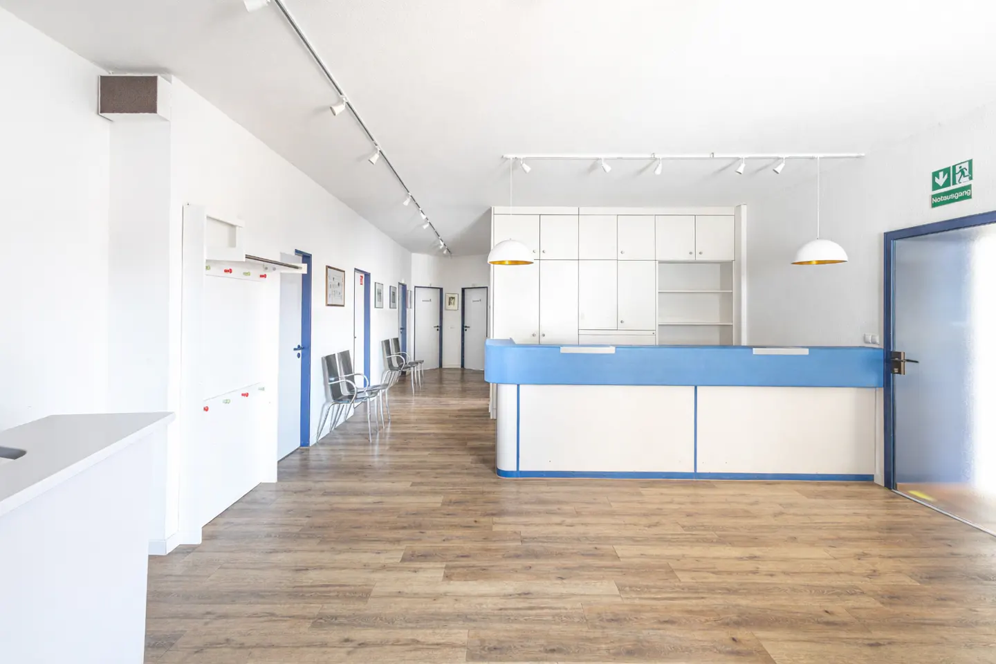 Bright waiting room with wood floors, white walls, and blue trim. A reception desk and chairs line the hallway.