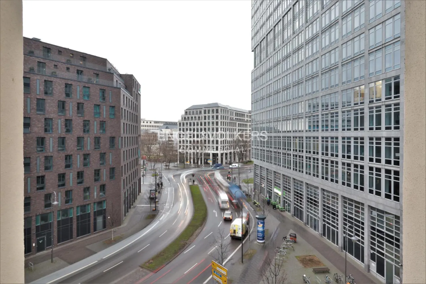 View from a high-rise building overlooking a city street with blurred car lights, modern brick and glass buildings.