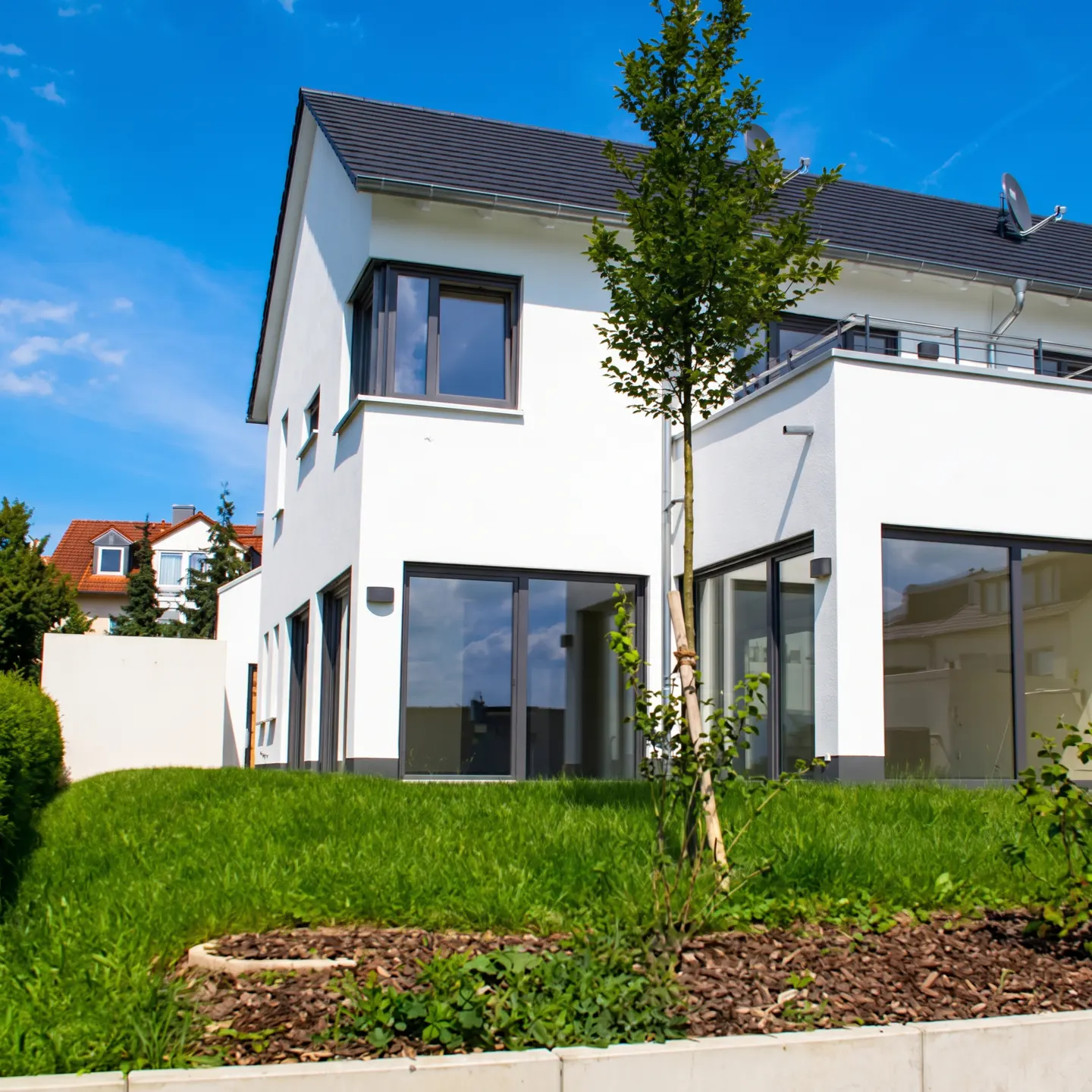 Modern white house with dark gray trim and roof, green lawn, and blue sky.