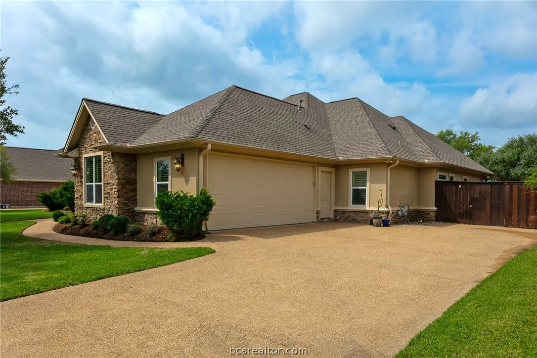 Beige single-story house with a brown roof, stone accents, and a two-car garage on a sunny day.