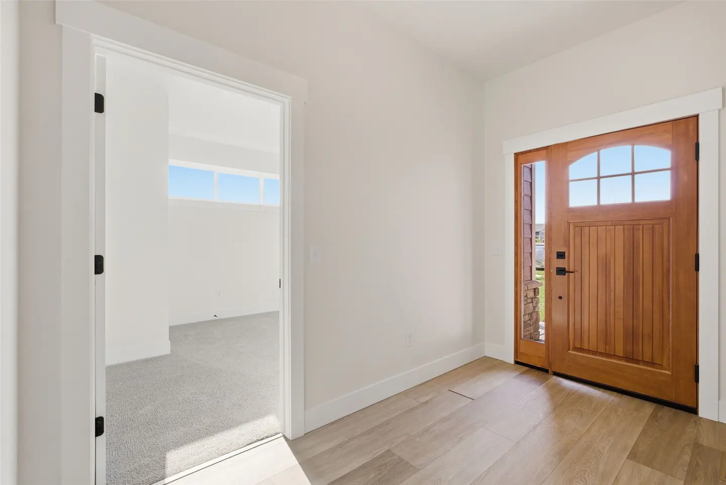Entryway with a wood front door with glass panes, light wood floors, and an open doorway to a carpeted room.