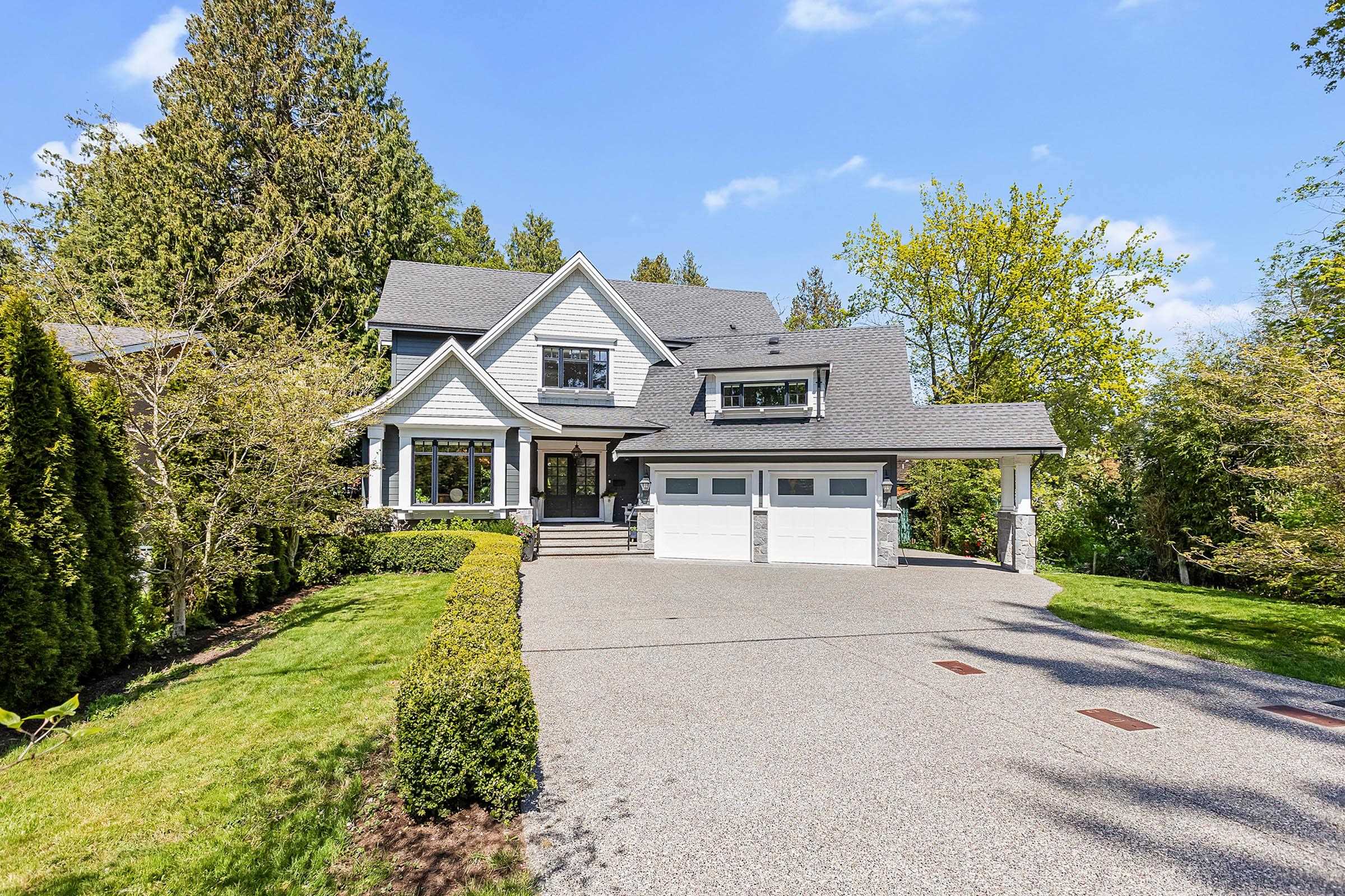 Two-story house with gray siding, white trim, and a gray roof. A two-car garage is attached to the house. A long driveway leads to the garage.