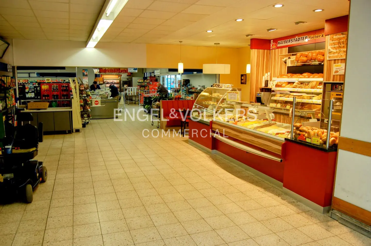 Interior view of a grocery store with a bakery section. Shelves of bread and pastries are visible. A mobility scooter is parked in the aisle.