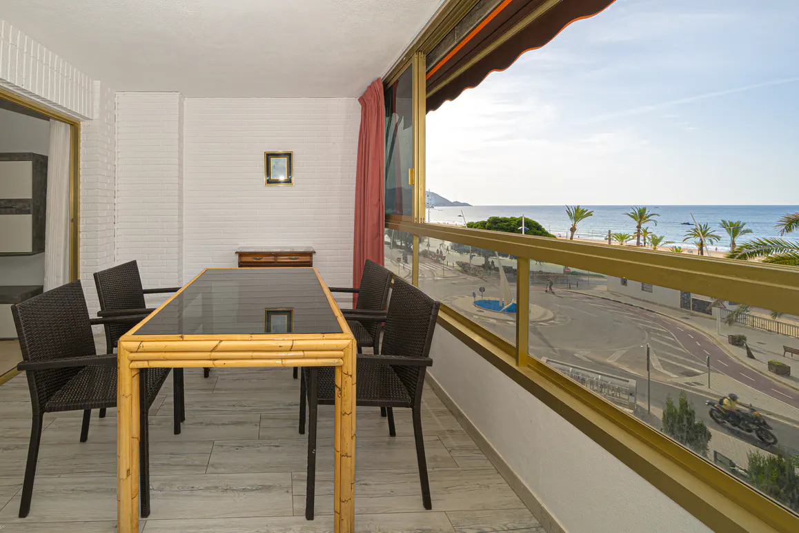 Balcony with a bamboo table, black chairs, and a view of the beach with palm trees.