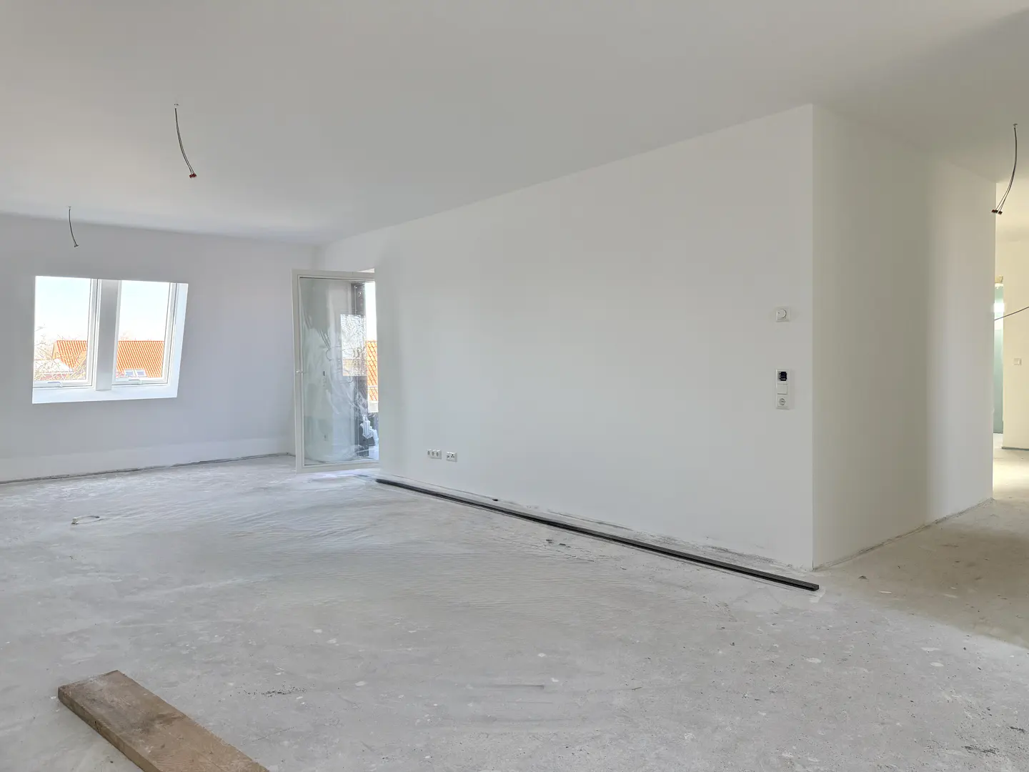 Unfinished room with white walls, concrete floor, window, and open doorway. Electrical wires hang from the ceiling.