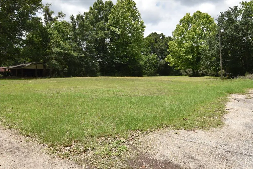 A grassy lot with trees in the background and a building on the left.