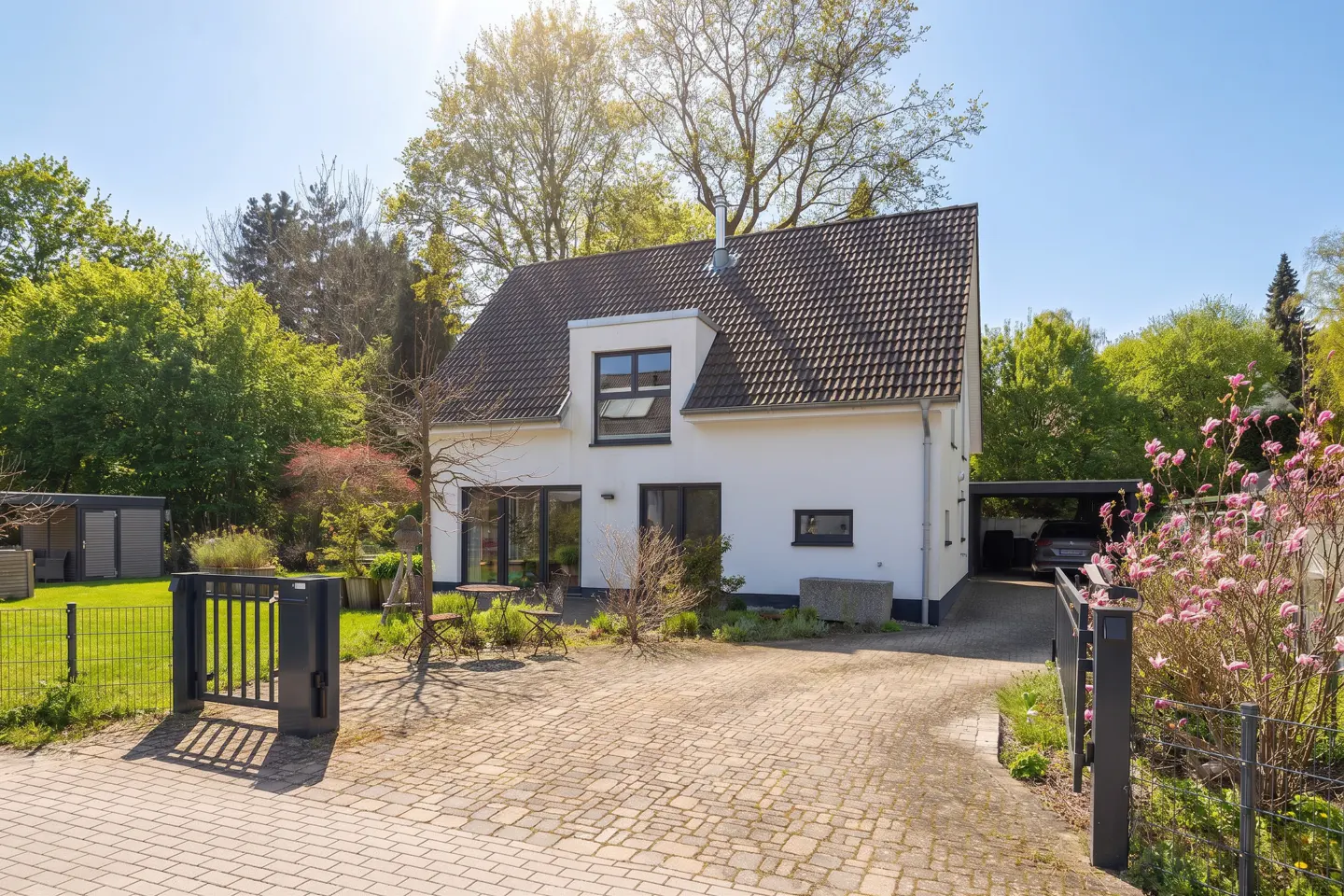 Exterior view of a two-story white house with a brown roof, a driveway, and green trees.