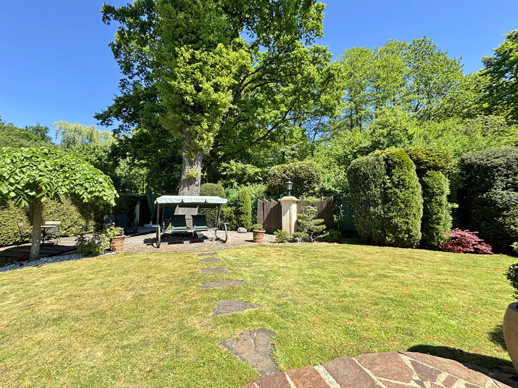 A lush green backyard with a swing, trees, and stone path under a clear blue sky.