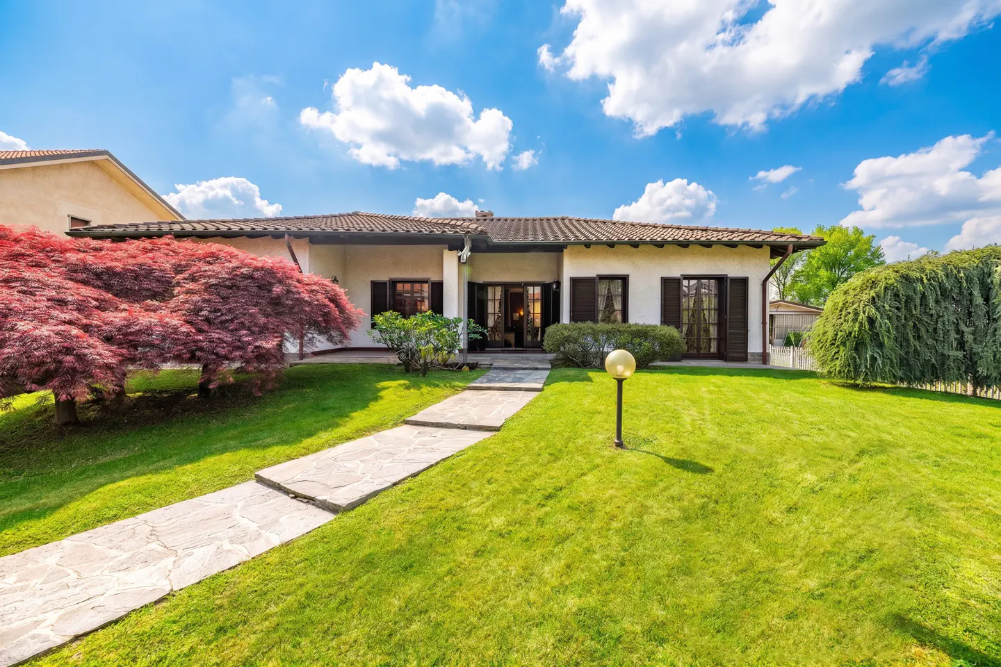 Exterior of a one-story white house with brown shutters, a stone walkway, and a green lawn under a blue sky.