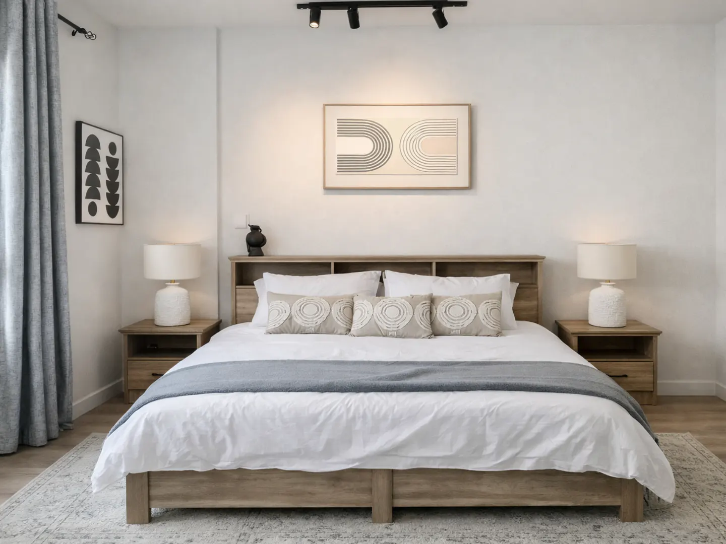 Modern bedroom with a wooden bed, white bedding, grey runner, matching nightstands, lamps, and abstract wall art.