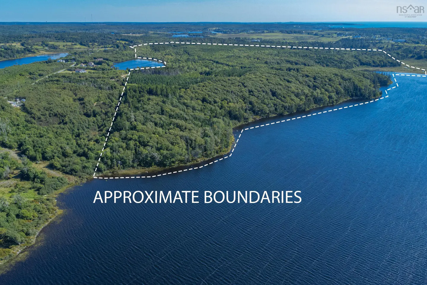 Aerial view of land for sale, bordered in white, with lake frontage and dense green trees. "Approximate Boundaries" text overlay.