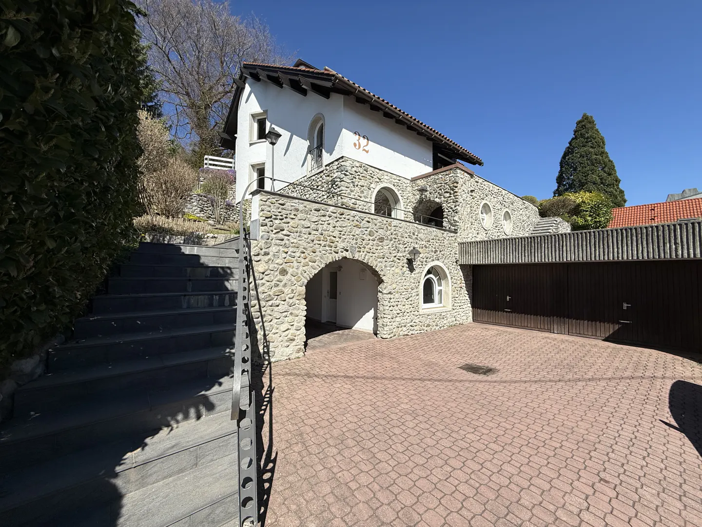 Exterior view of a two-story house with stone accents, a red brick driveway, and a staircase leading up to the house.
