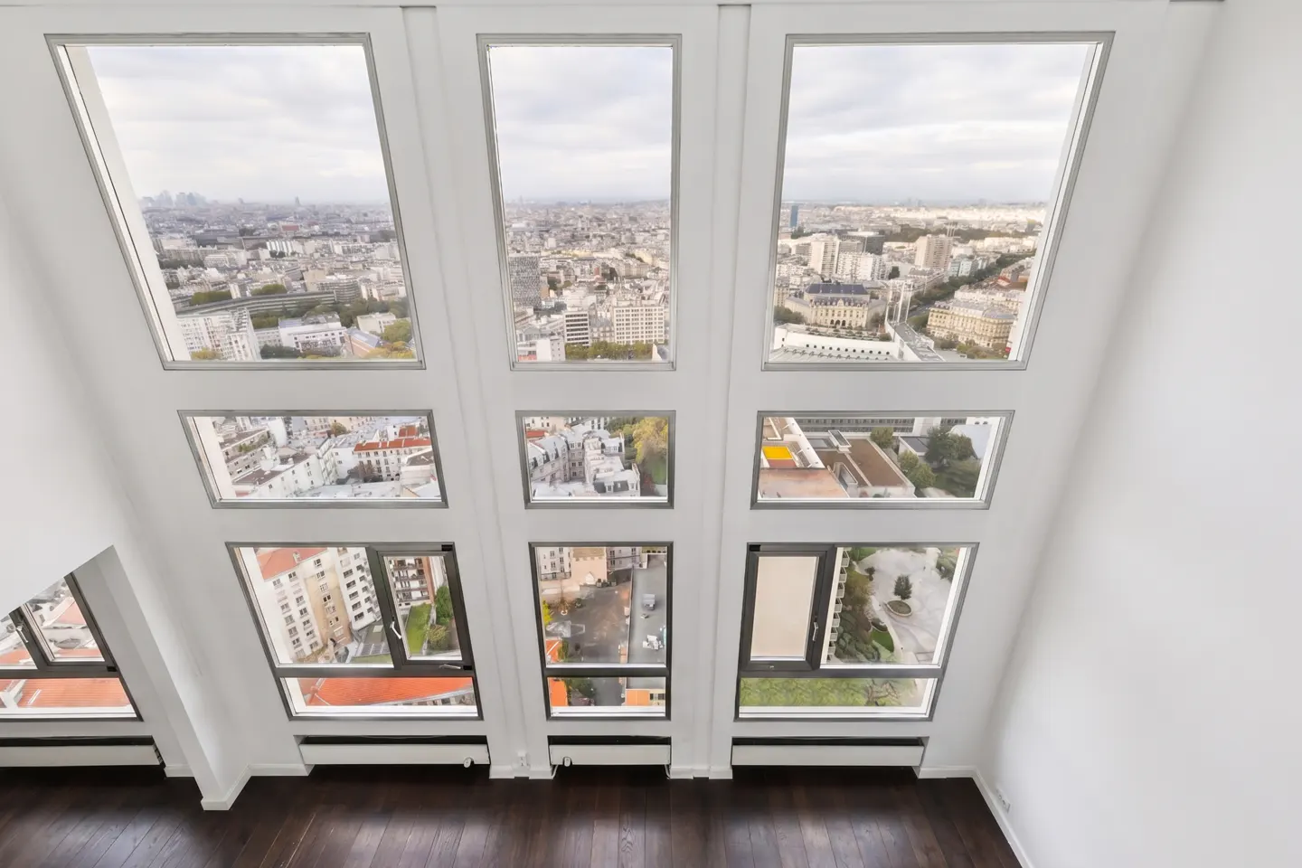 View from a bright, modern room with dark wood floors and nine windows showing a cityscape.