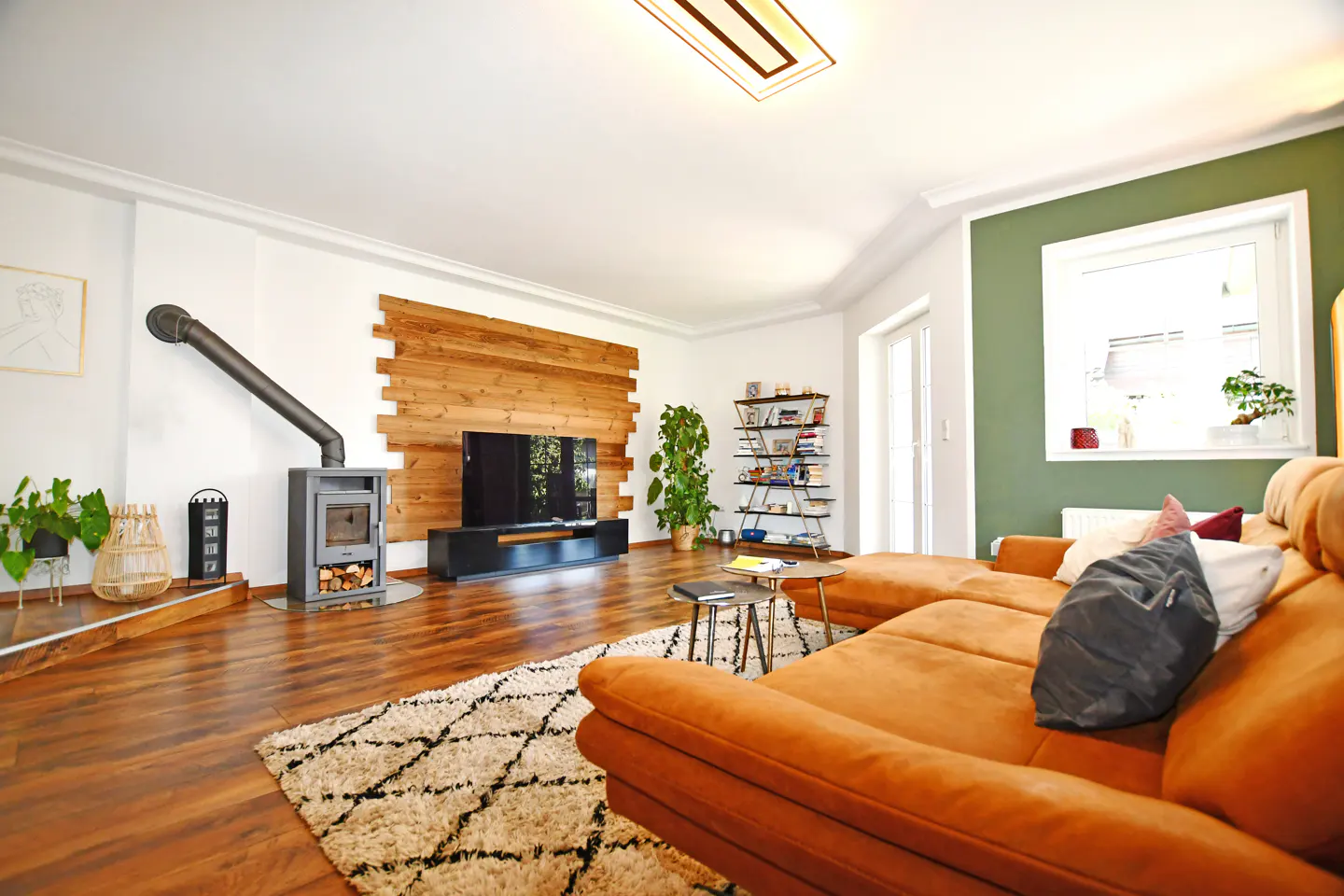 Modern living room with a brown sectional sofa, wood-paneled TV wall, fireplace, and green accent wall with a window.
