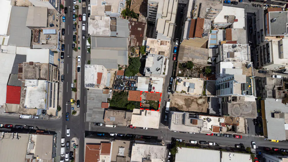 Aerial view of a city block with a red-outlined property lot featuring a small building and yard amidst surrounding buildings.