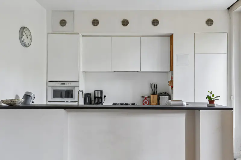 A bright, modern kitchen with white cabinets, a black countertop, and stainless steel appliances. A clock hangs on the wall.