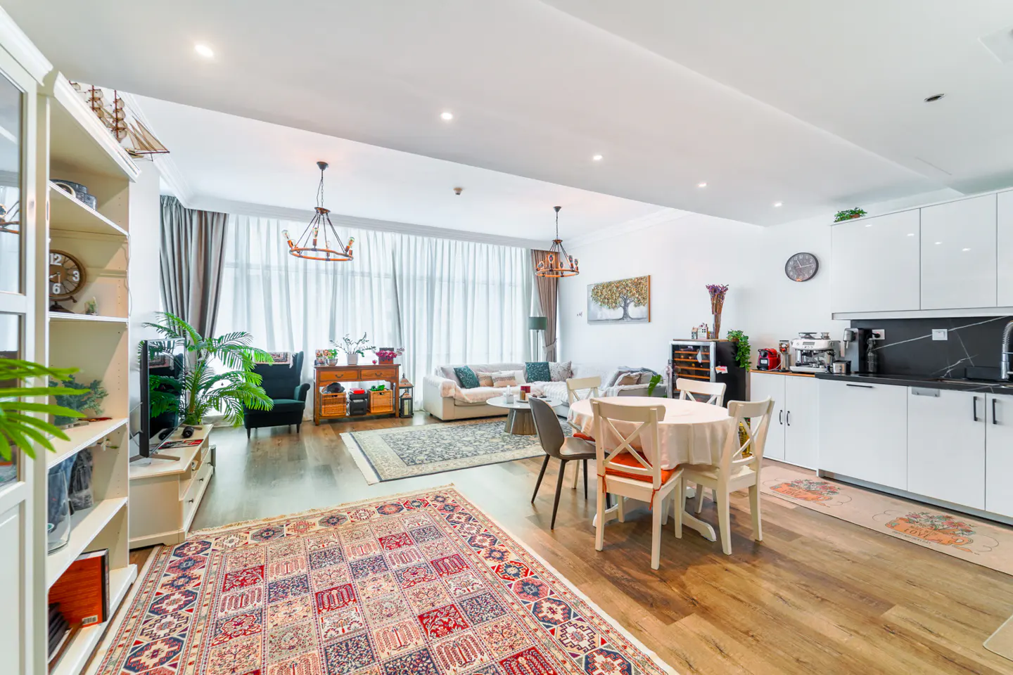 Bright, open-concept living space with white walls, wood floors, and rugs. Includes a kitchen, dining area, and living room.