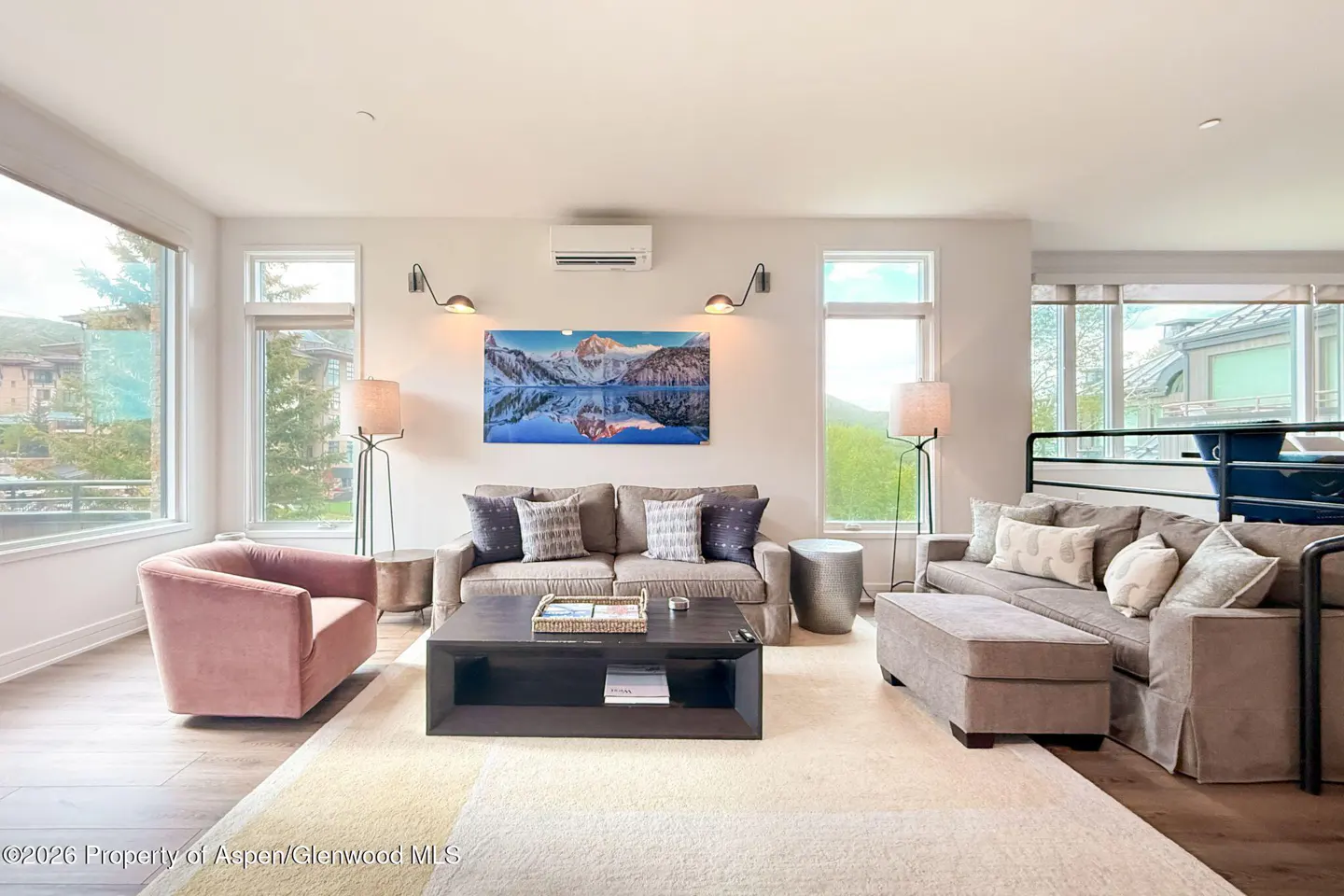 Modern living room with a pink armchair, grey sofa, coffee table, and a mountain landscape painting on the wall.